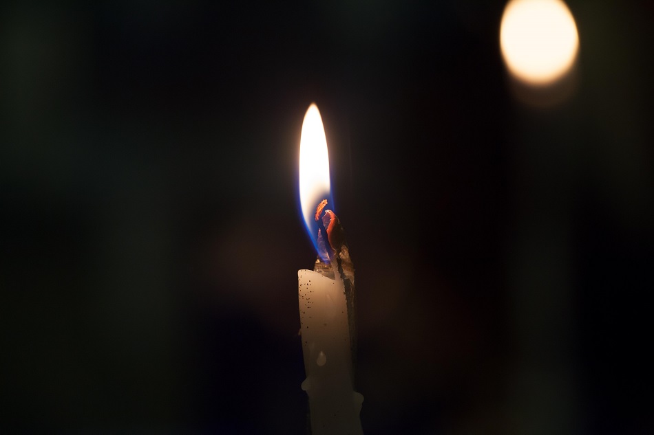 a lone candle shines against a dark backdrop