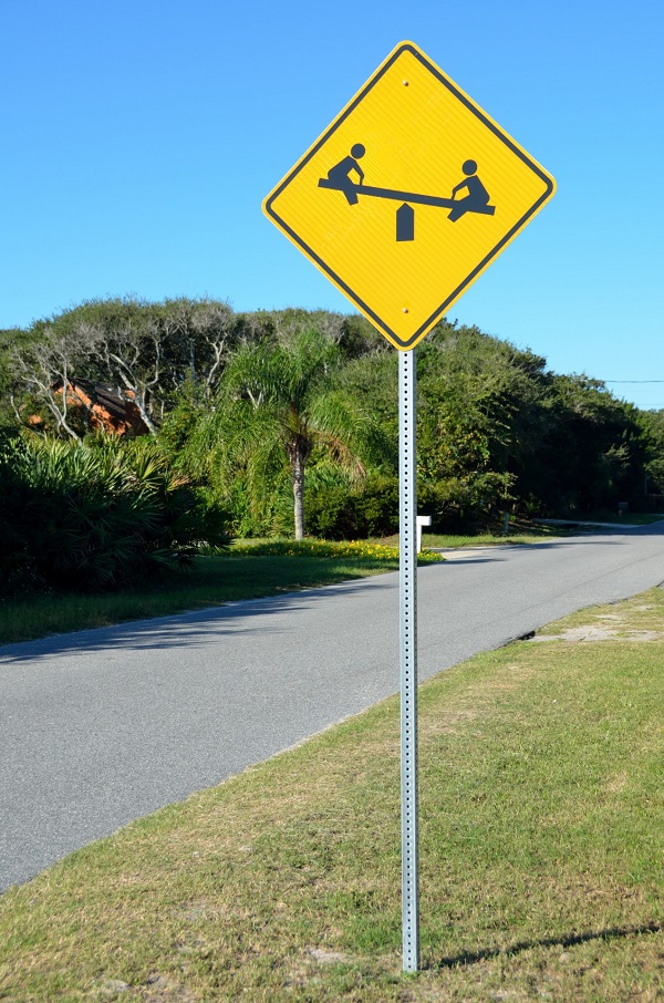 a sign beside a road depicts children playing